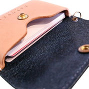 Close-up of an open leather pocket case with a blue interior and tan flap, showcasing business cards neatly stored inside and featuring gold snap and ring hardware.