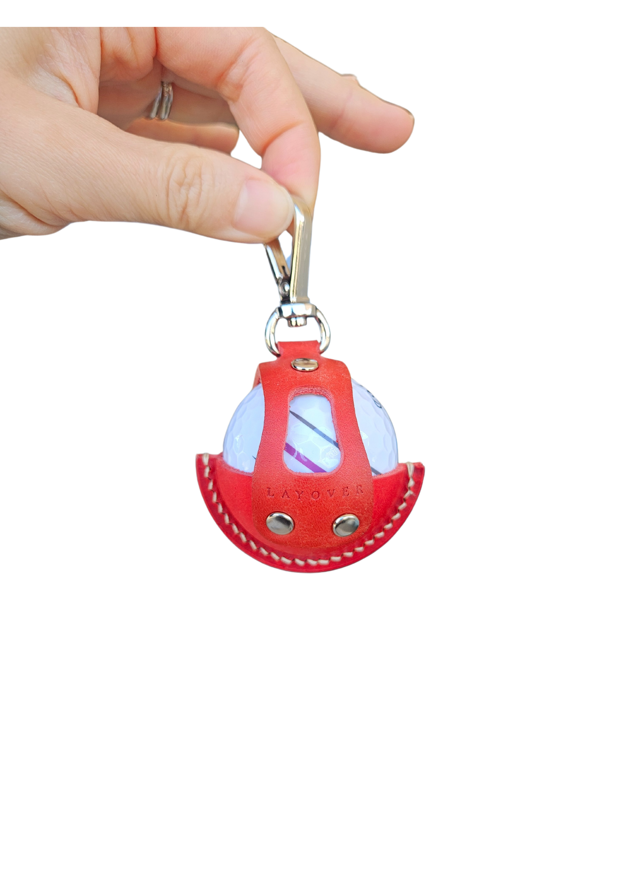 A close-up of a red leather golf ball holder with visible stitching and metallic rivets, held by a hand. The holder features a secure clip at the top and an open-front design showcasing a white golf ball inside
